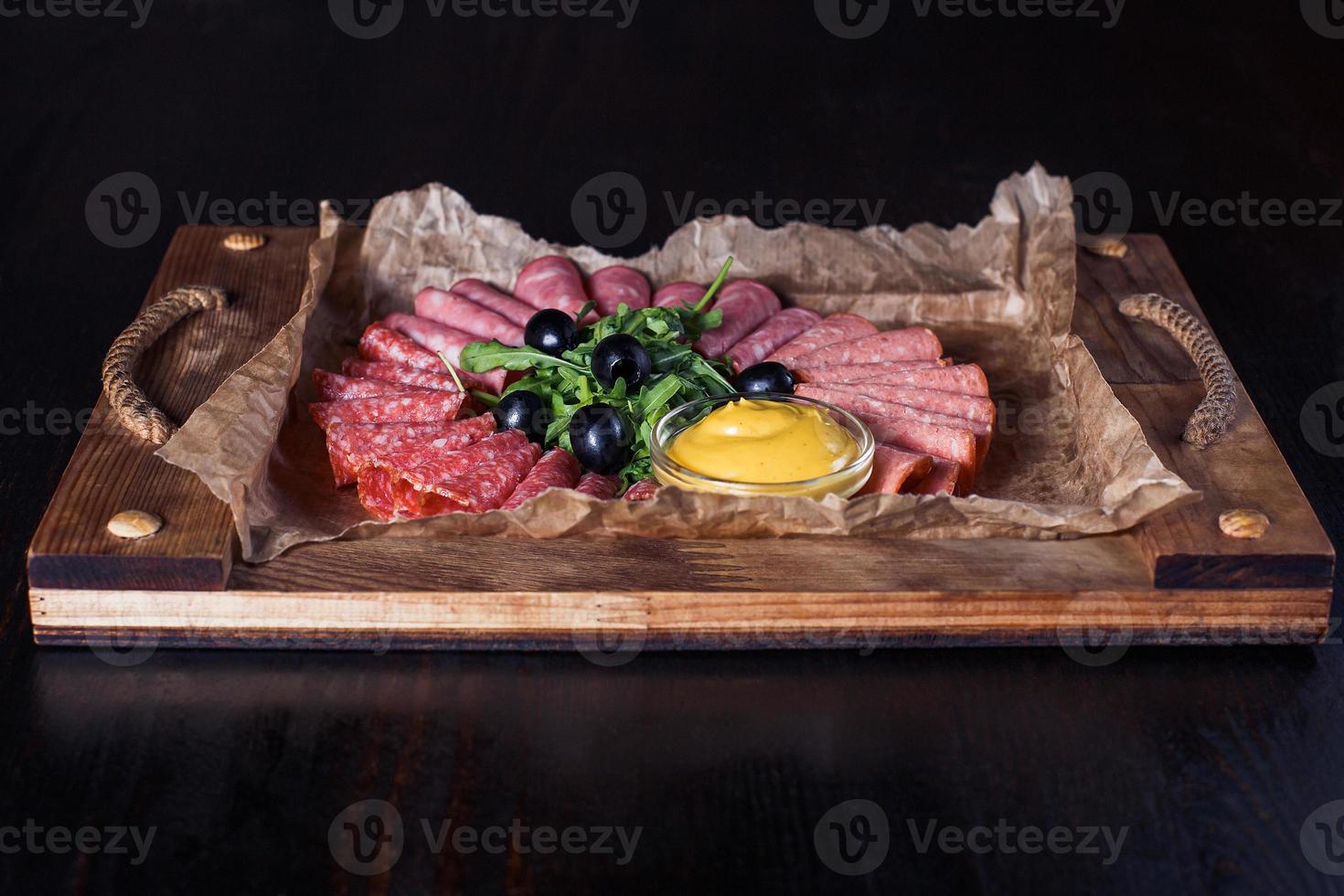 Wurst geschnitten mit Kräutern und Soße auf einem Holztablett, schöne Portion, dunkler Hintergrund foto