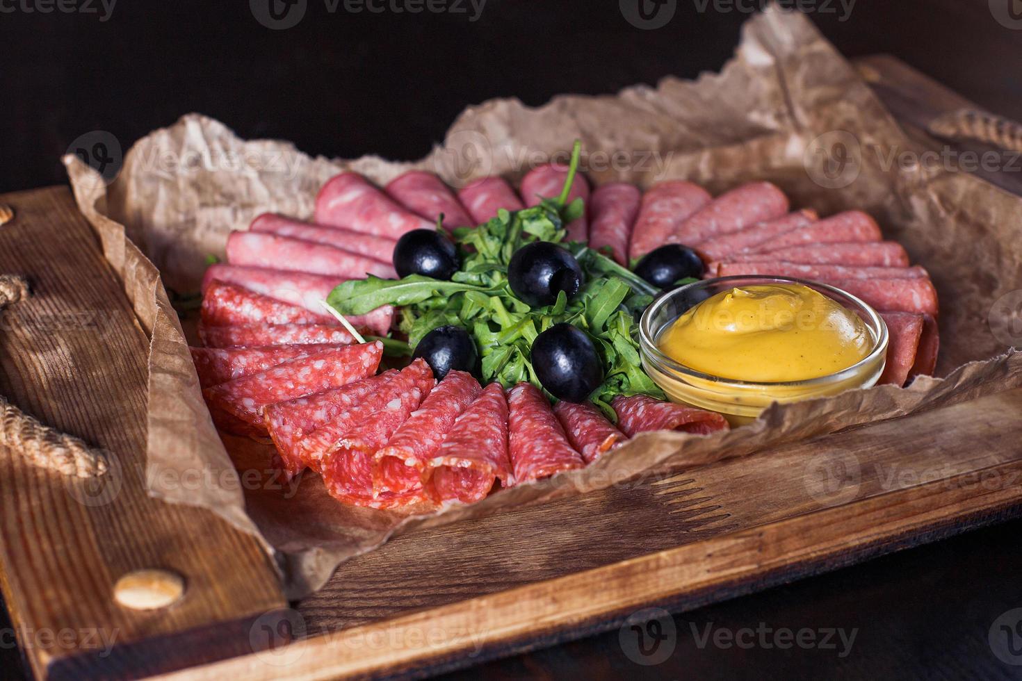 Wurst geschnitten mit Kräutern und Soße auf einem Holztablett, schöne Portion, dunkler Hintergrund foto