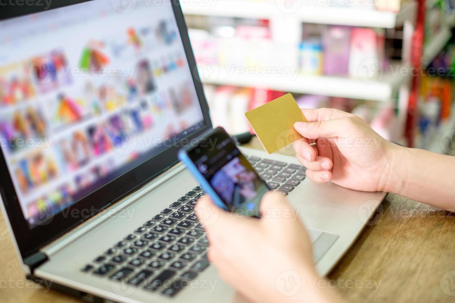 Hand, die Kreditkarte hält und Laptop mit Smartphone für Online-Zahlungen verwendet foto