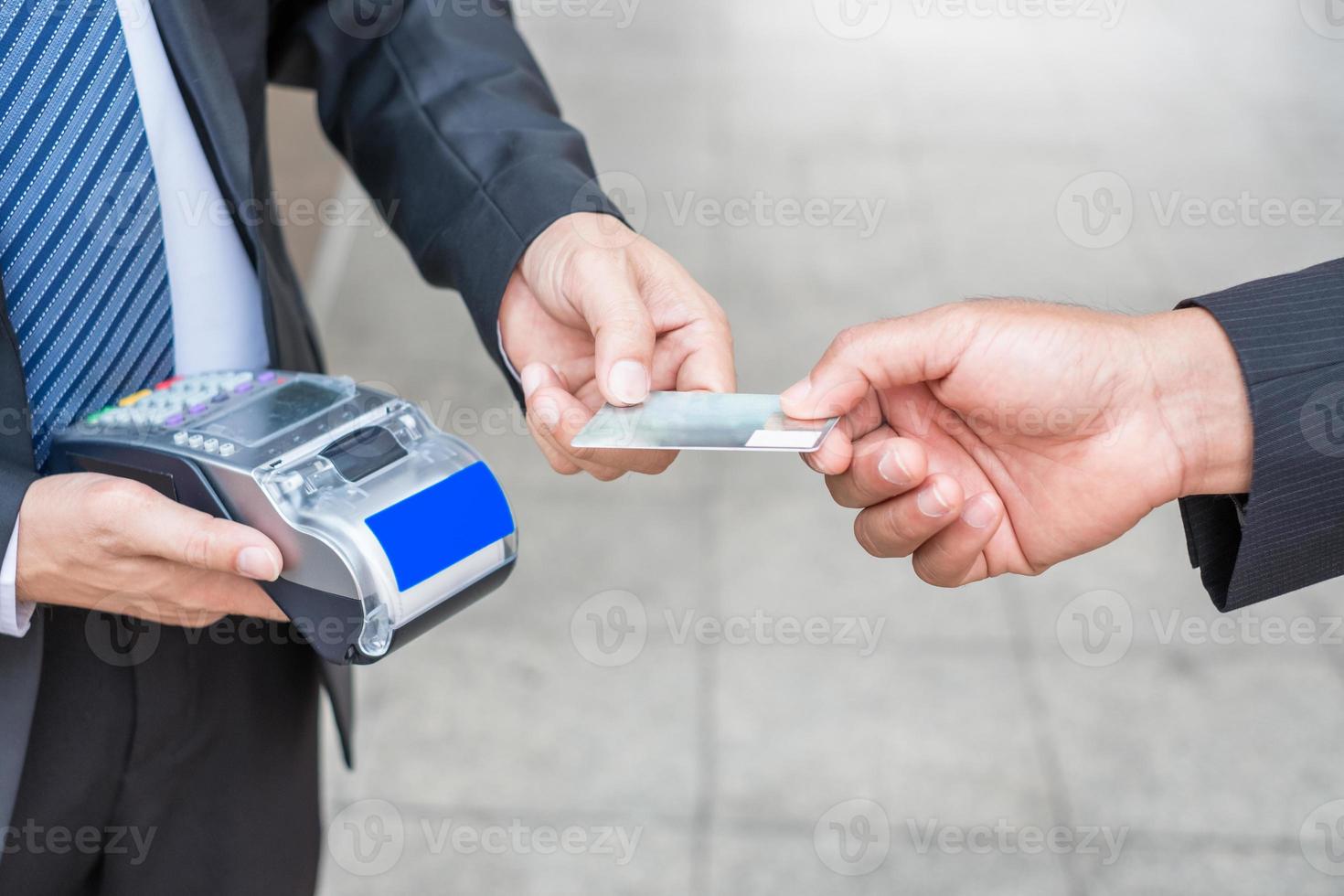 Hand, die Kreditkarte mit Geschäftsmann mit Zahlungsterminal hält foto