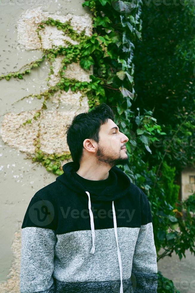 ein junger attraktiver mann in ruhiger stellung mit geschlossenen augen den kopf und draußenpflanzen hinter ihm foto