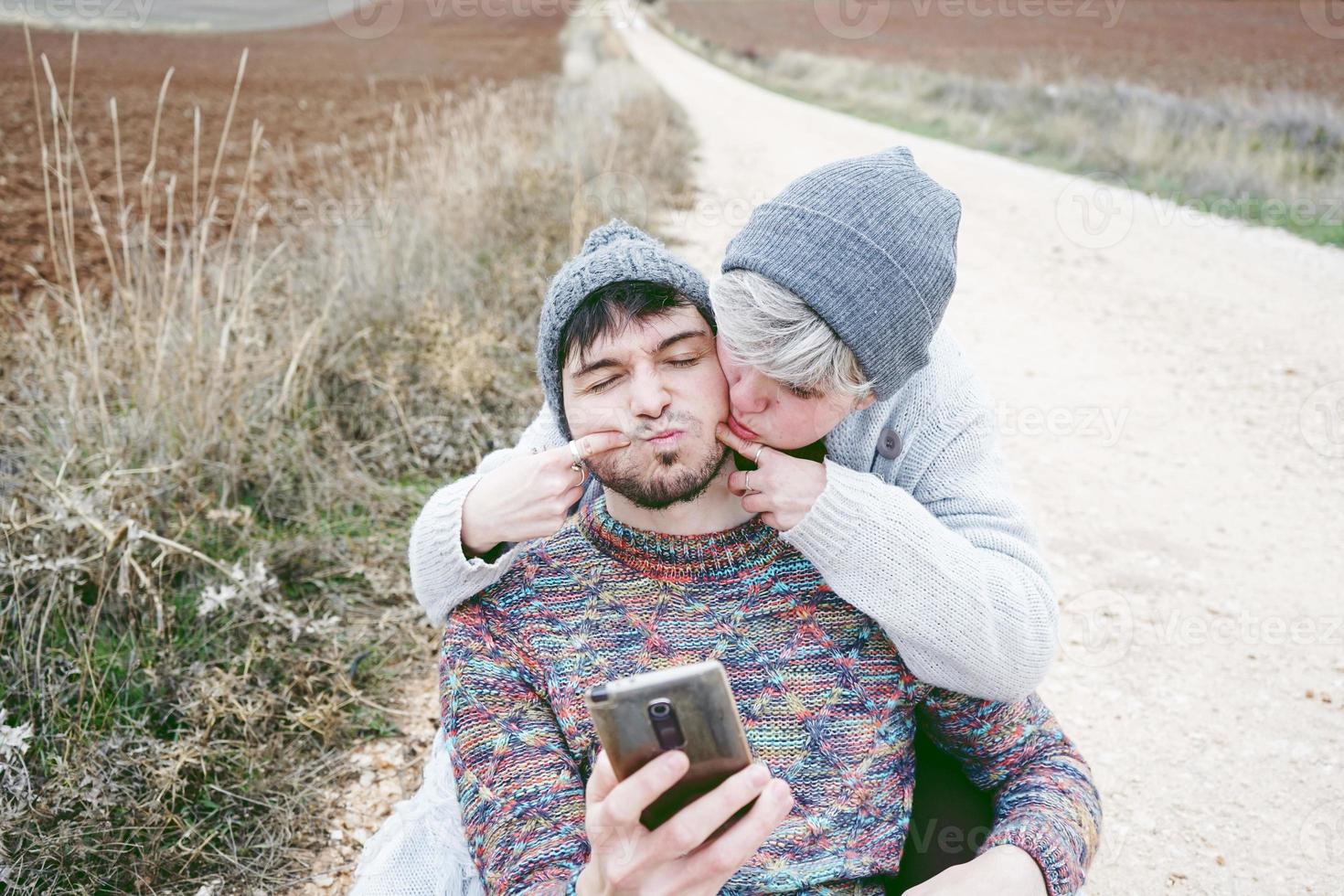 Ein paar junge Millennials machen Spaß und scherzen mit lustigem Ausdruck vor einem Smartphone bei einer Abenteuerreise auf einem Feldweg im Freien foto