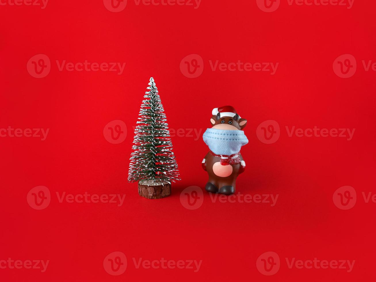 Keramikstatuette von Ochsen in medizinischer Maske und Weihnachtsbaum auf rotem Hintergrund. Symbol des neuen Jahres 2021. foto