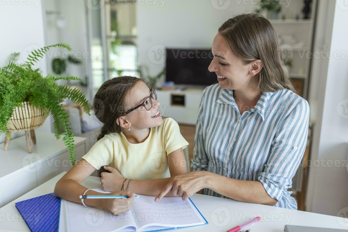 Mutter Portion ihr Tochter während studieren beim heim. ziemlich lächelnd Frau Portion bezaubernd Tochter tun Schularbeit beim Zuhause foto