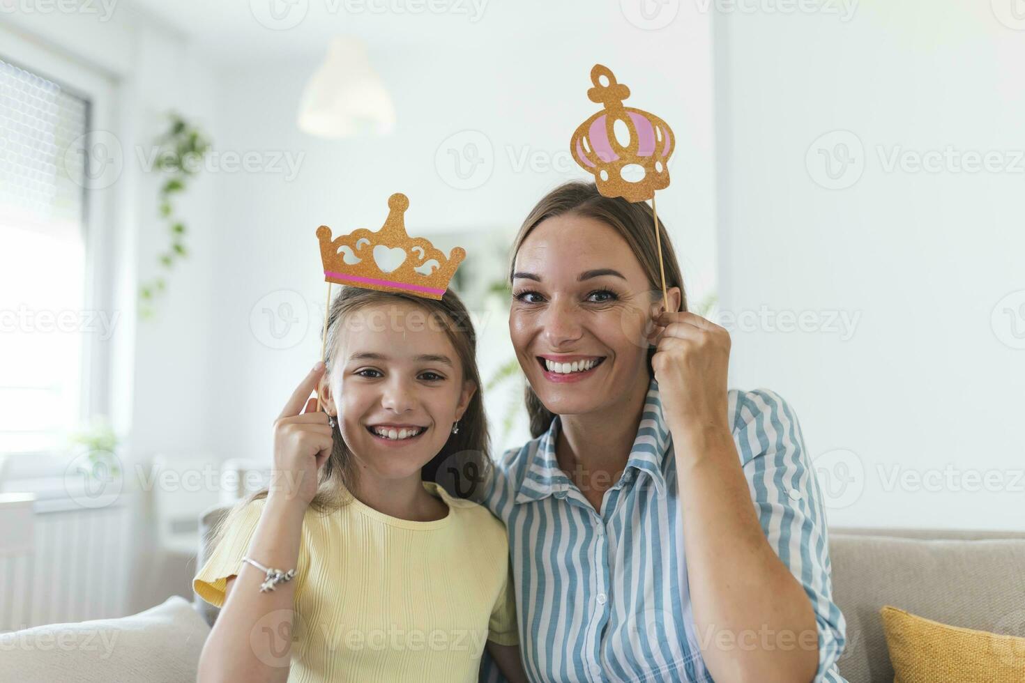 komisch Familie auf ein Hintergrund von hell Mauer. Mutter und ihr Tochter Mädchen mit ein Papier Zubehör. Mama und Kind sind halten Papier Krone auf Stock. foto