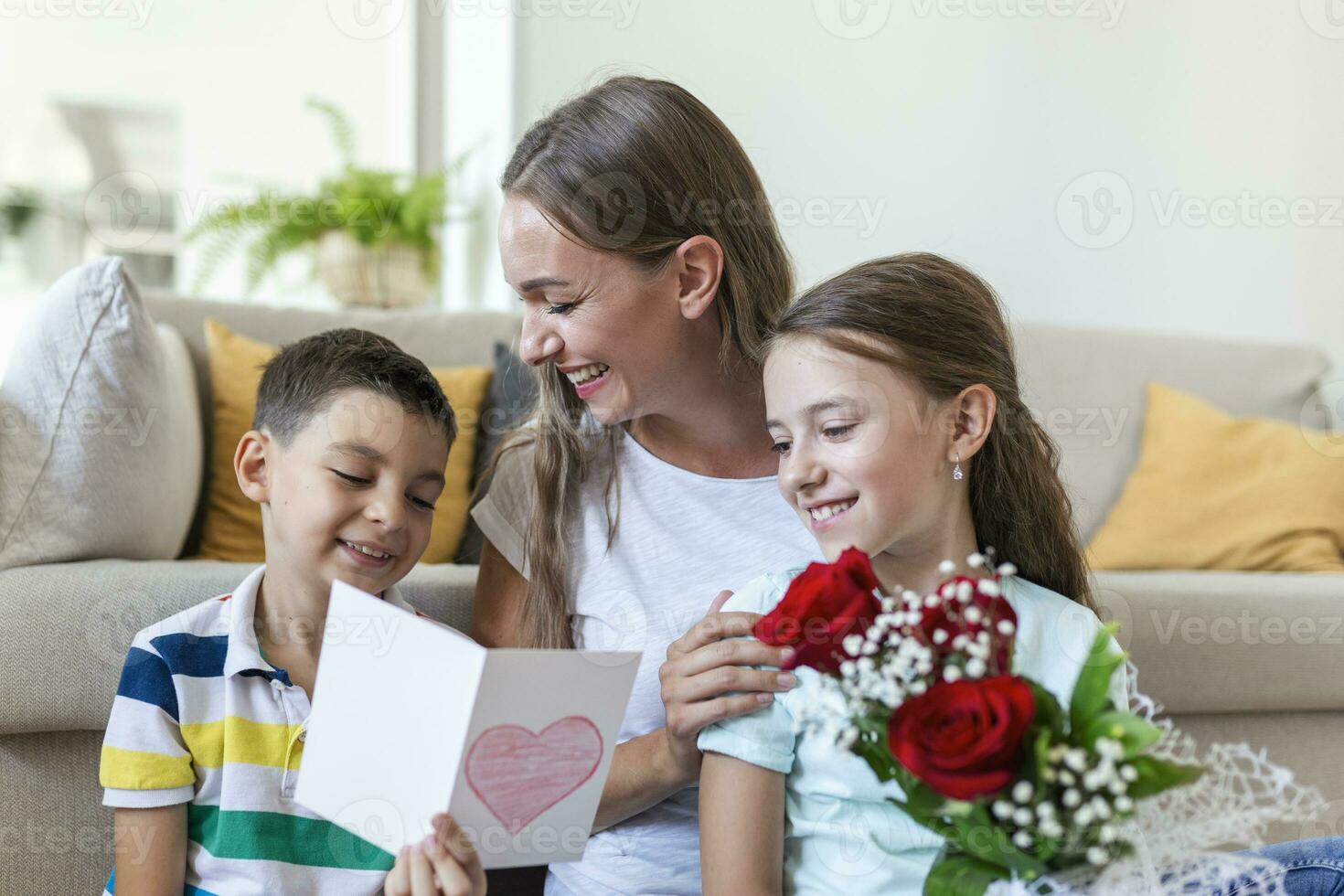 jung Mutter mit ein Strauß von Rosen lacht, umarmen ihr Sohn, und heiter Mädchen mit ein Karte und Rosen gratuliert Mama während Urlaub Feier beim heim. foto