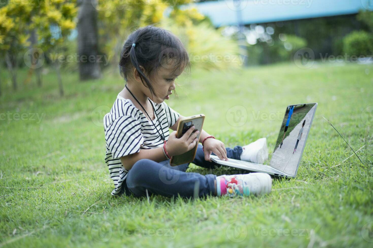 glücklich asiatisch Familie Picknick. Töchter spielen Handy, Mobiltelefon Telefone und Laptops haben Spaß zusammen während Sitzung allein auf sonnig Tag. foto