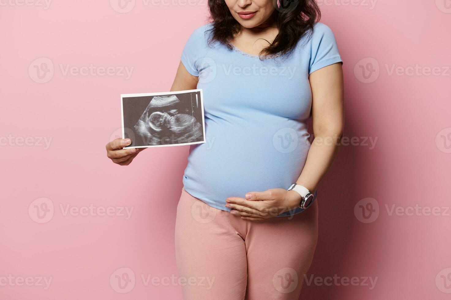 Nahansicht Studio Schuss von das Bauch von ein schwanger Frau zeigen Ultraschall Scan von ihr Baby Über isoliert Rosa Hintergrund. foto