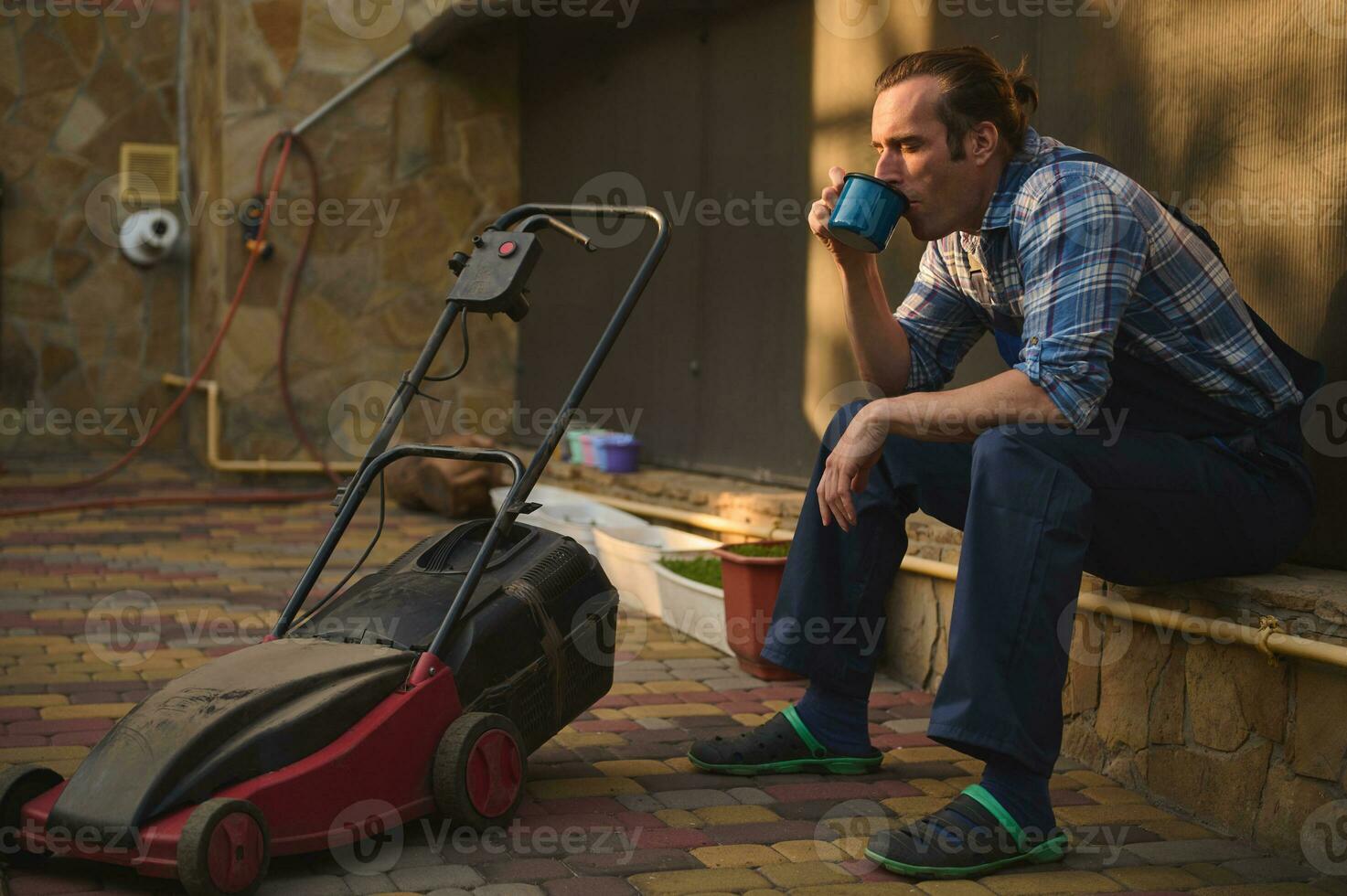 Fachmann Gärtner im Blau Gartenarbeit Overall und Plaid Shirt, nehmen ein brechen nach schwer Arbeiten Tag im das Garten foto