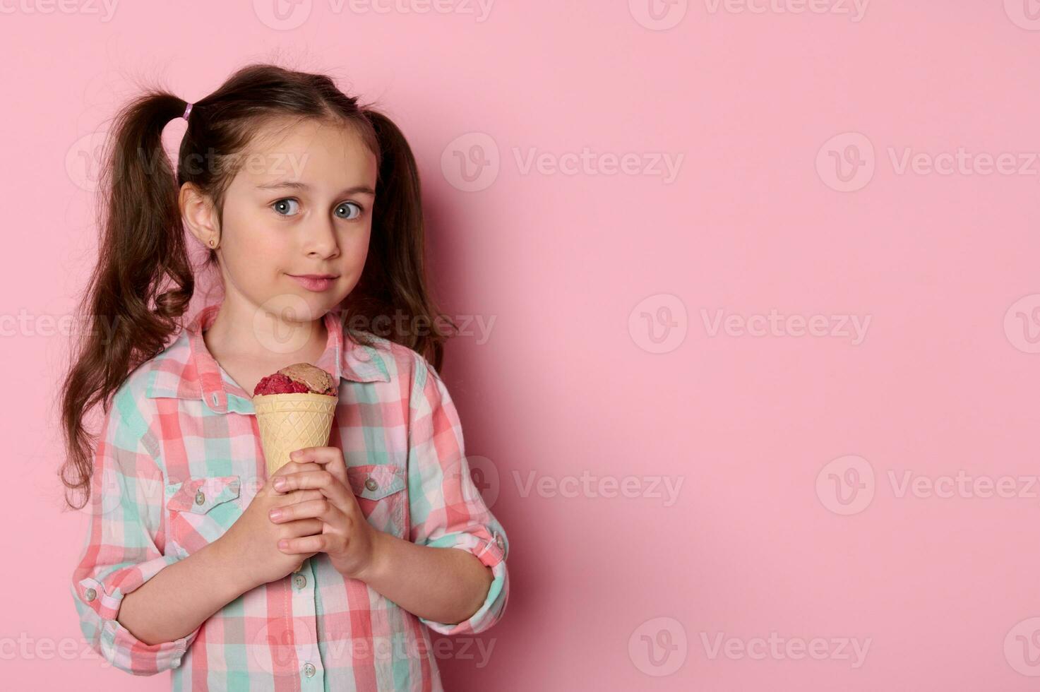 schön Blau Augen wenig Kind Mädchen lächelnd suchen beim Kamera, halten ein Waffel Kegel mit Eis Creme, auf Rosa Hintergrund foto