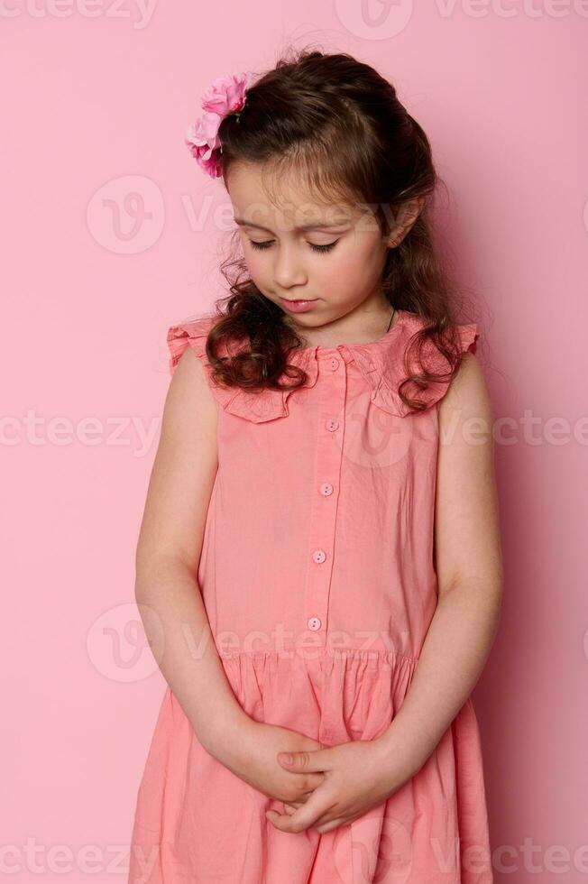 schön Kokette, schüchtern wenig Mädchen 5-6 Jahre alt, Stehen Über Rosa isoliert Hintergrund. Kinder Mode und Schönheit foto