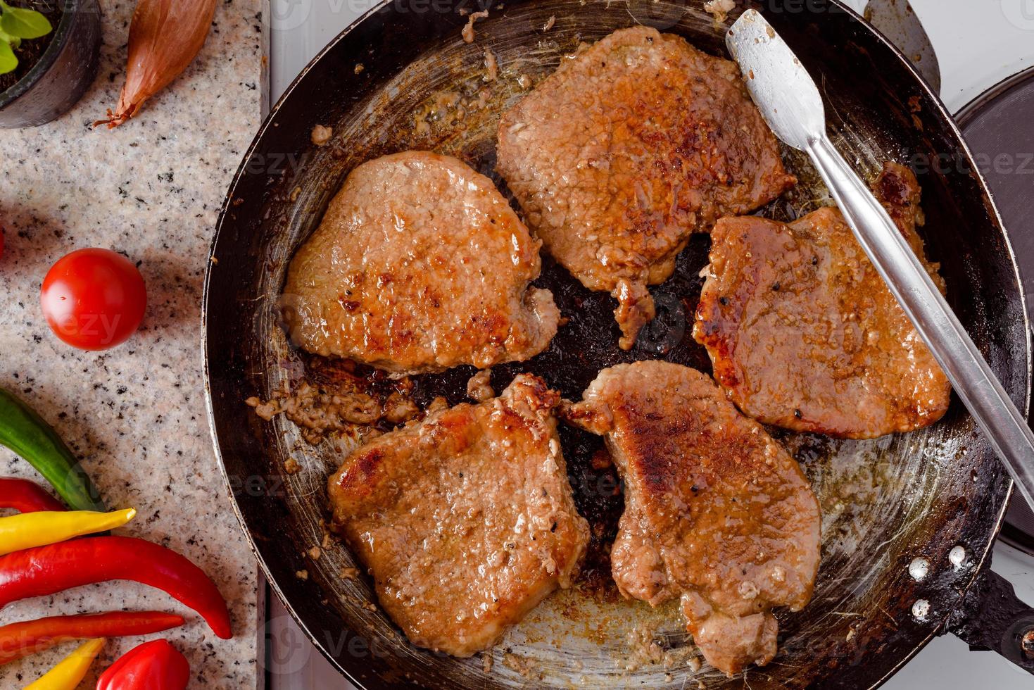 Schweinesteakbraten auf rustikaler Pfanne, frische scharfe Chilischoten, Tomaten und Kräuter. foto