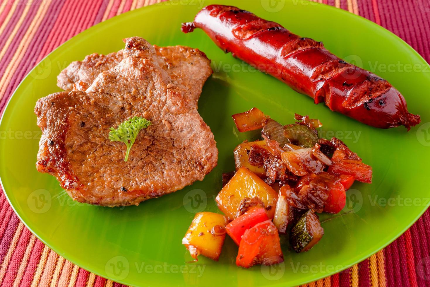 Schweinesteak, Wurst und gebratenes, gegrilltes Gemüse auf dem Teller. foto