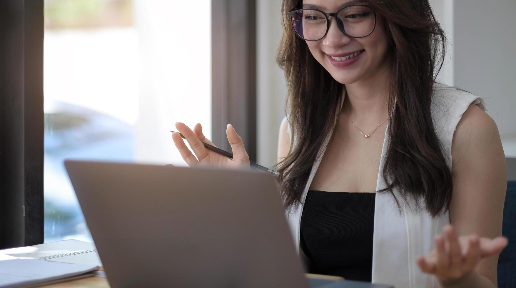 Porträt einer glücklichen jungen asiatischen Frau, die zu Hause lächelt und eine Gruppenvideokonferenz auf dem Laptop hat. freiberufliche Frau, die während des Online-Meetings von zu Hause aus auf einem Laptop arbeitet foto