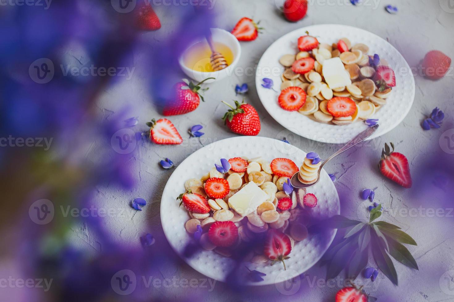 Pfannkuchen-Müsli, trendiges Essen. Mini-Getreidepfannkuchen mit Butter, Honig und Erdbeeren. foto