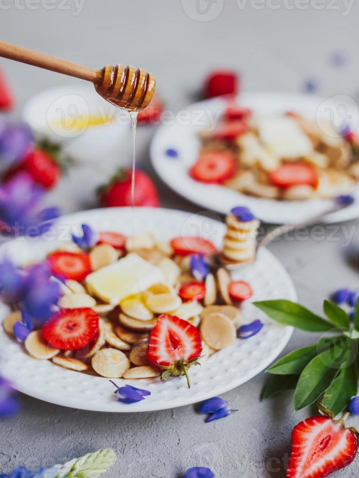 Pfannkuchen-Müsli, trendiges Essen. Mini-Getreidepfannkuchen mit Butter, Honig und Erdbeeren. foto