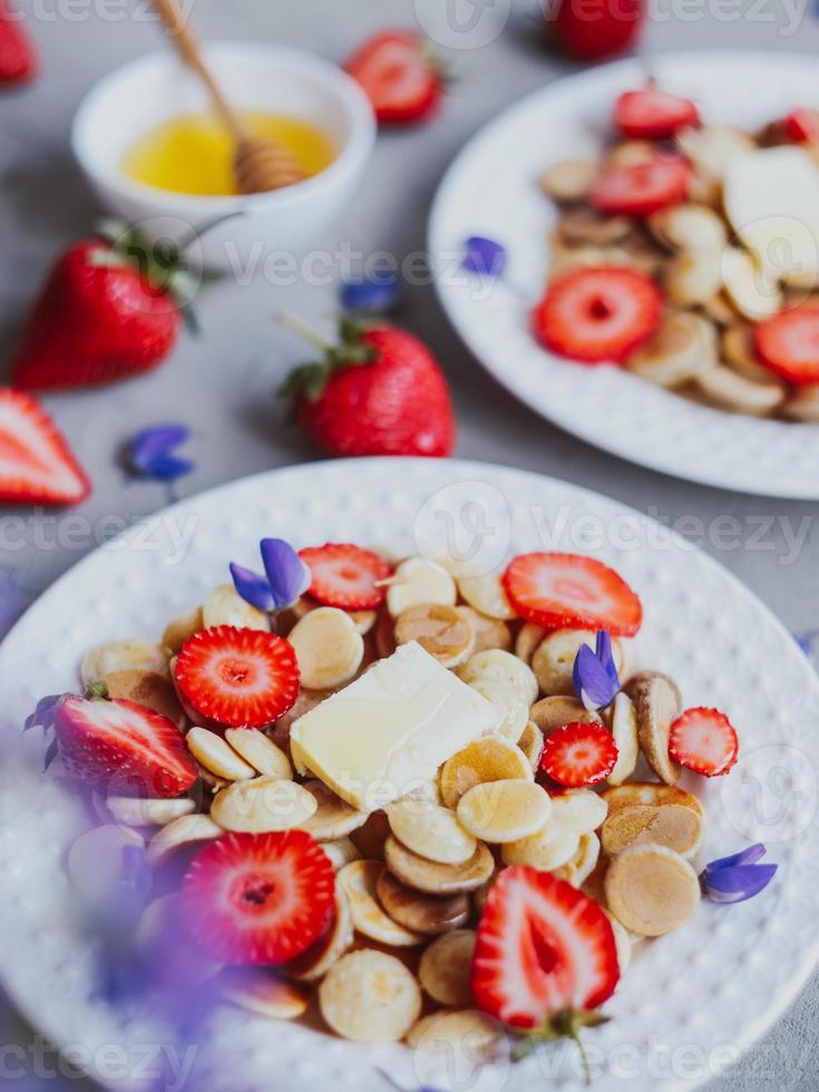 Pfannkuchen-Müsli, trendiges Essen. Mini-Getreidepfannkuchen mit Butter, Honig und Erdbeeren. foto