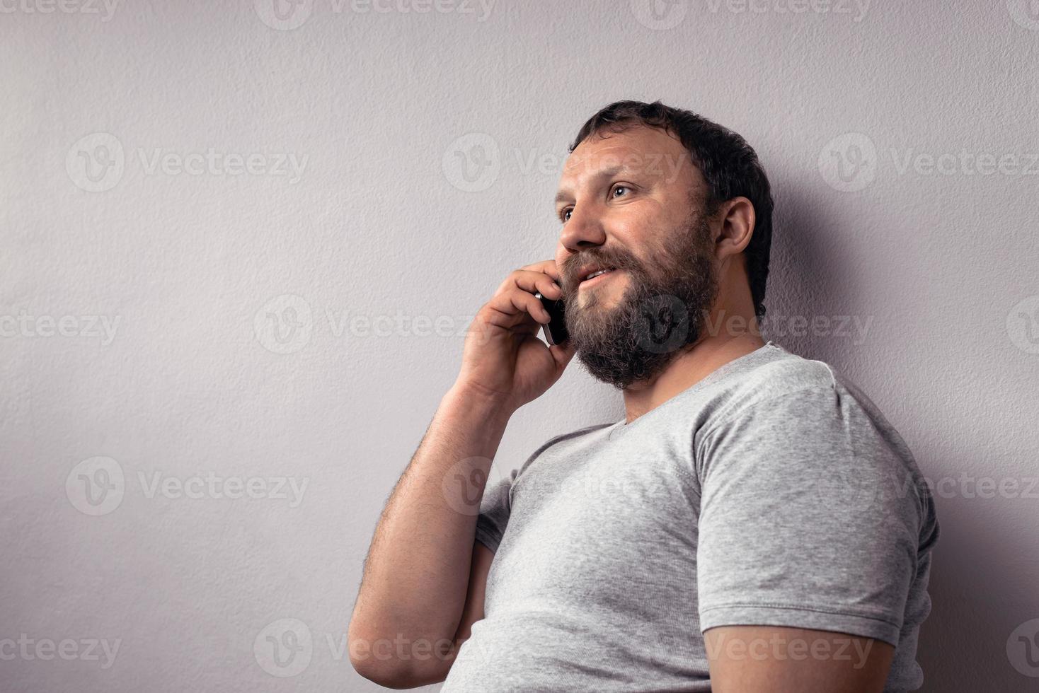 bärtiger Mann im grauen T-Shirt mit Handy foto