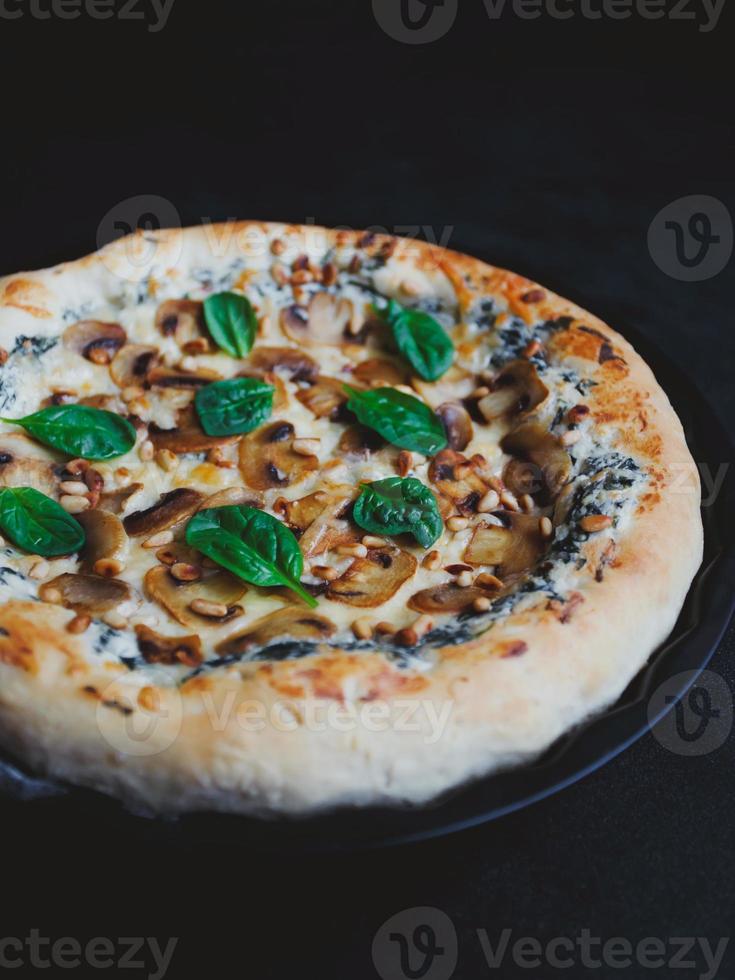 hausgemachte Pizza mit Pilzen, Spinat, Knoblauch, Frischkäse und Pinienkernen, auf dunklem Hintergrund. foto