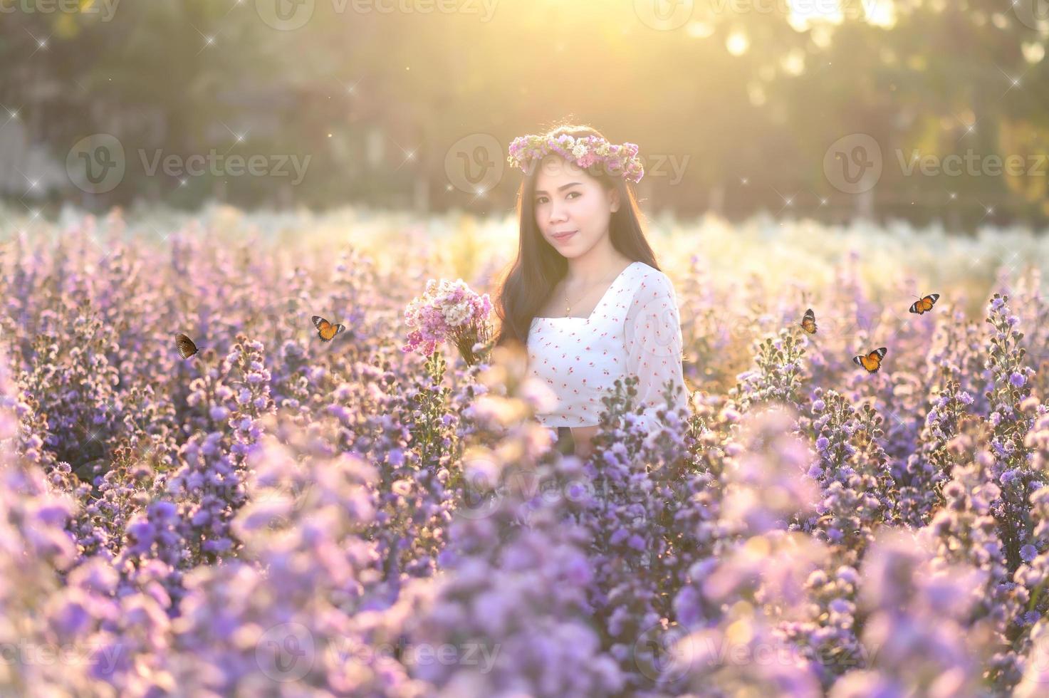 eine frau, die blumen in einem blumenfeld mit schmetterlingen am abend beobachtet, oranges licht. foto