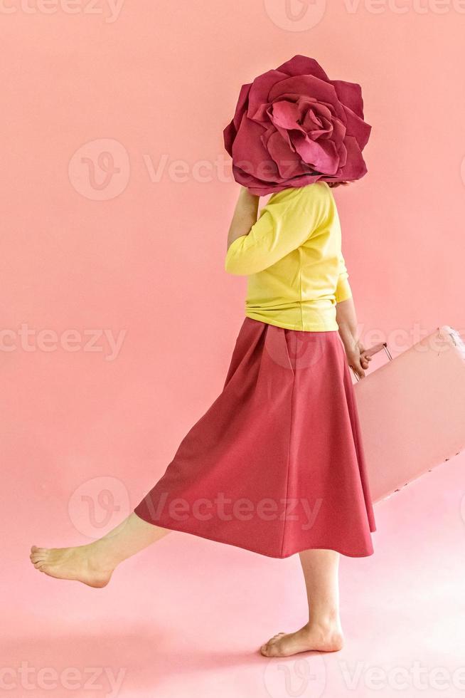 eine junge frau mit einem koffer in den händen und einer blume auf rosa hintergrund. das Konzept des Reisens in der Coronavirus-Pandemie foto