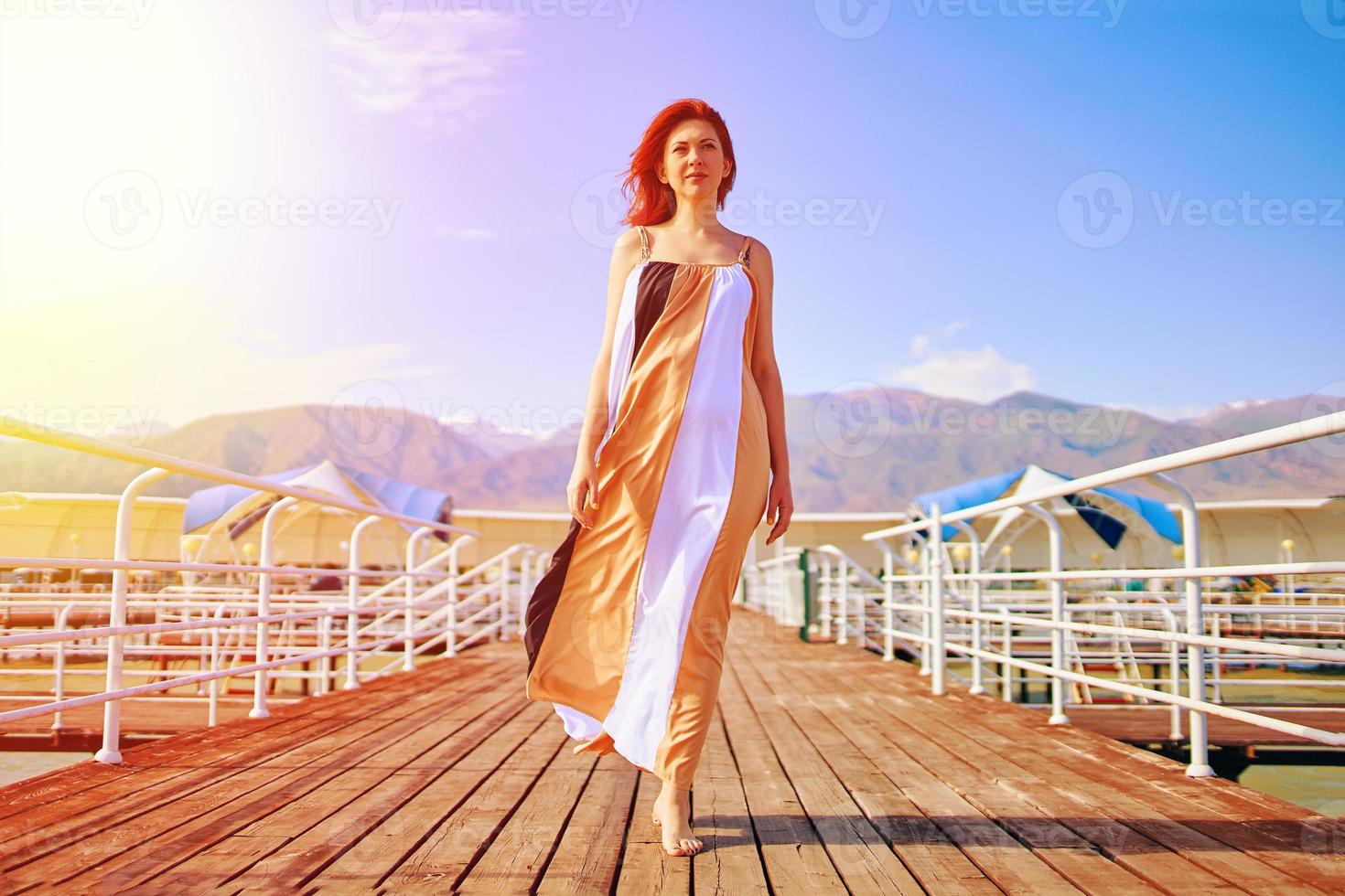 Rothaariges Mädchen posiert in einem flatternden Kleid auf dem Pier. foto