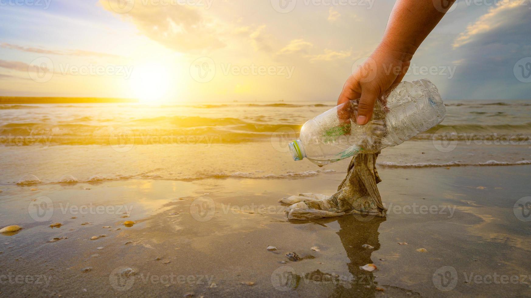 die Hand sammelt Müll am Strand auf, die Idee des Umweltschutzes foto