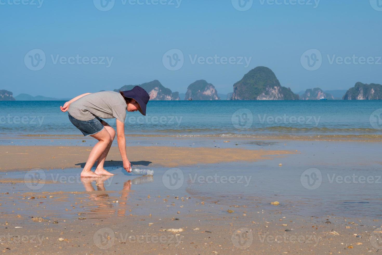 junge asiatische frau, die gebrauchte plastikflaschen vom strand sammelt, um die umwelt und das meeresökosystem zu retten foto