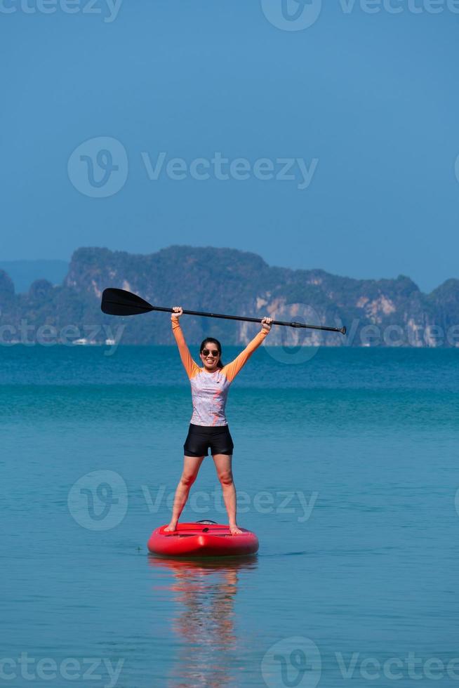 Junge sportliche Frau, die an einem sonnigen Tag der Sommerferien Stand-Up-Paddle-Board auf dem blauen Meer spielt foto