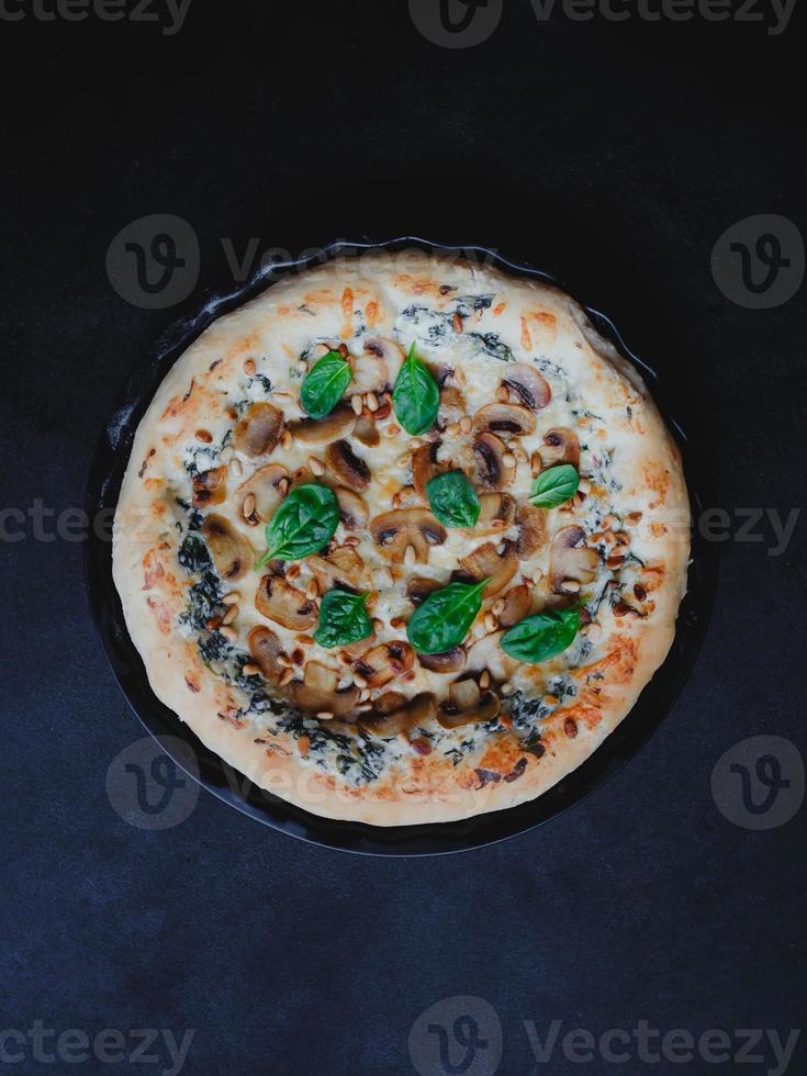 hausgemachte Pizza mit Pilzen, Spinat, Knoblauch, Frischkäse und Pinienkernen, auf dunklem Hintergrund. foto