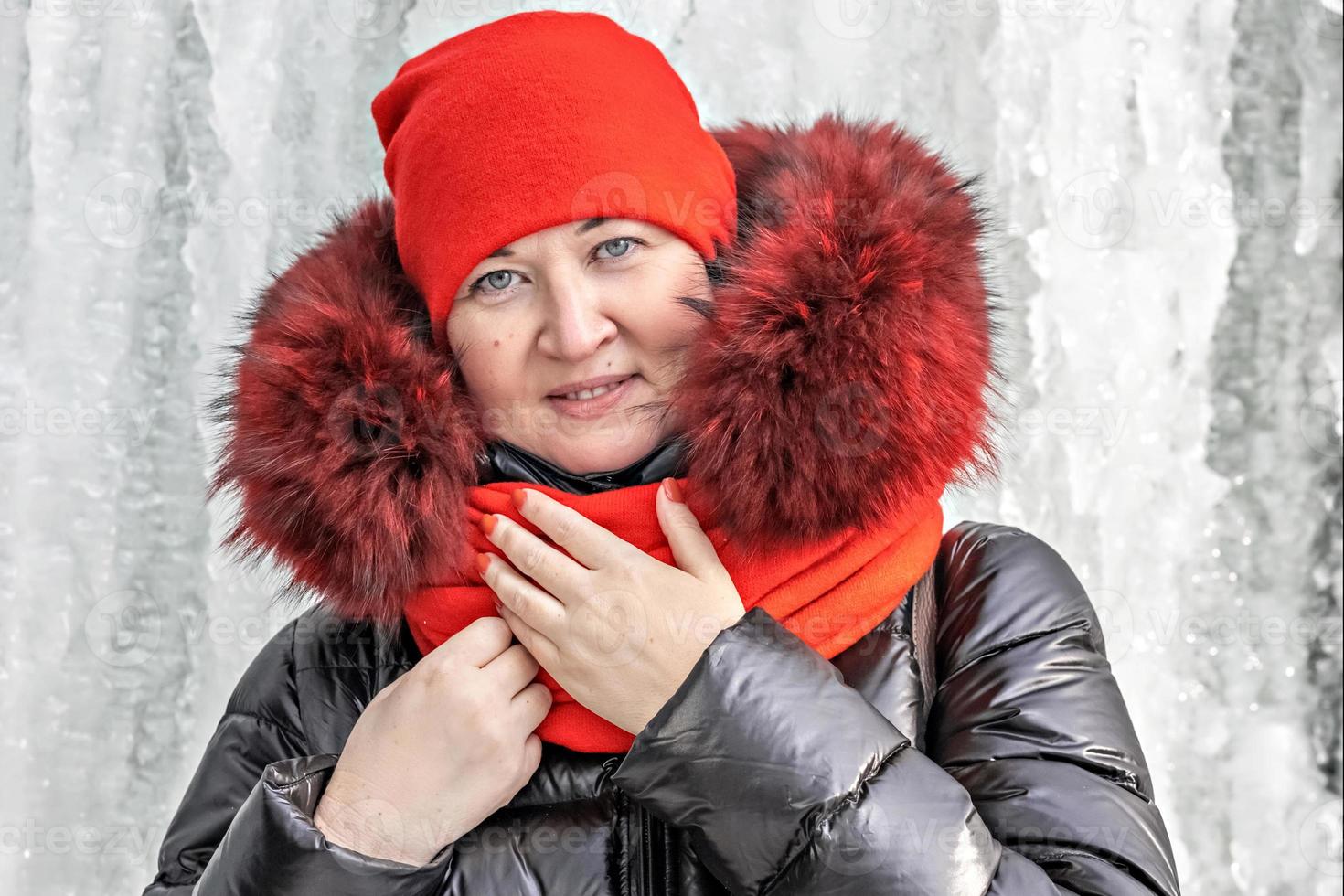 Porträt einer Frau mit rotem Hut und Schal, warme Jacke vor dem Hintergrund einer Eiswand. Winter foto