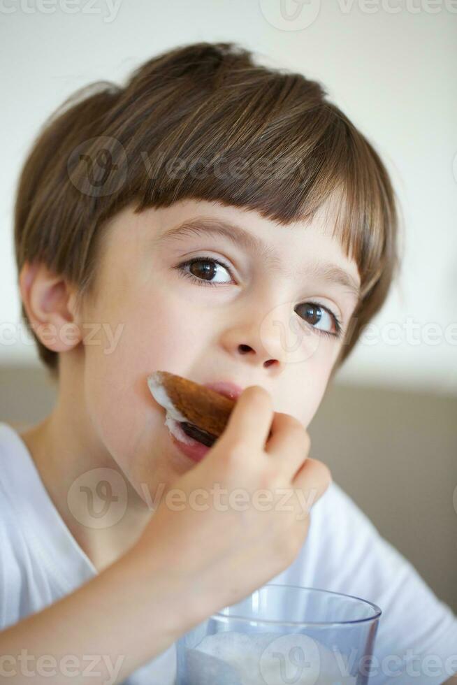 Junge von sechs Jahre ist nehmen ein Glas von warm Milch mit Hafer Kekse. foto