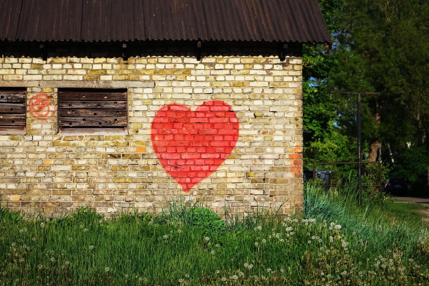 Graffiti malte großes rotes Herz auf gelber Backsteinmauer, umgeben von Gras und Bäumen foto
