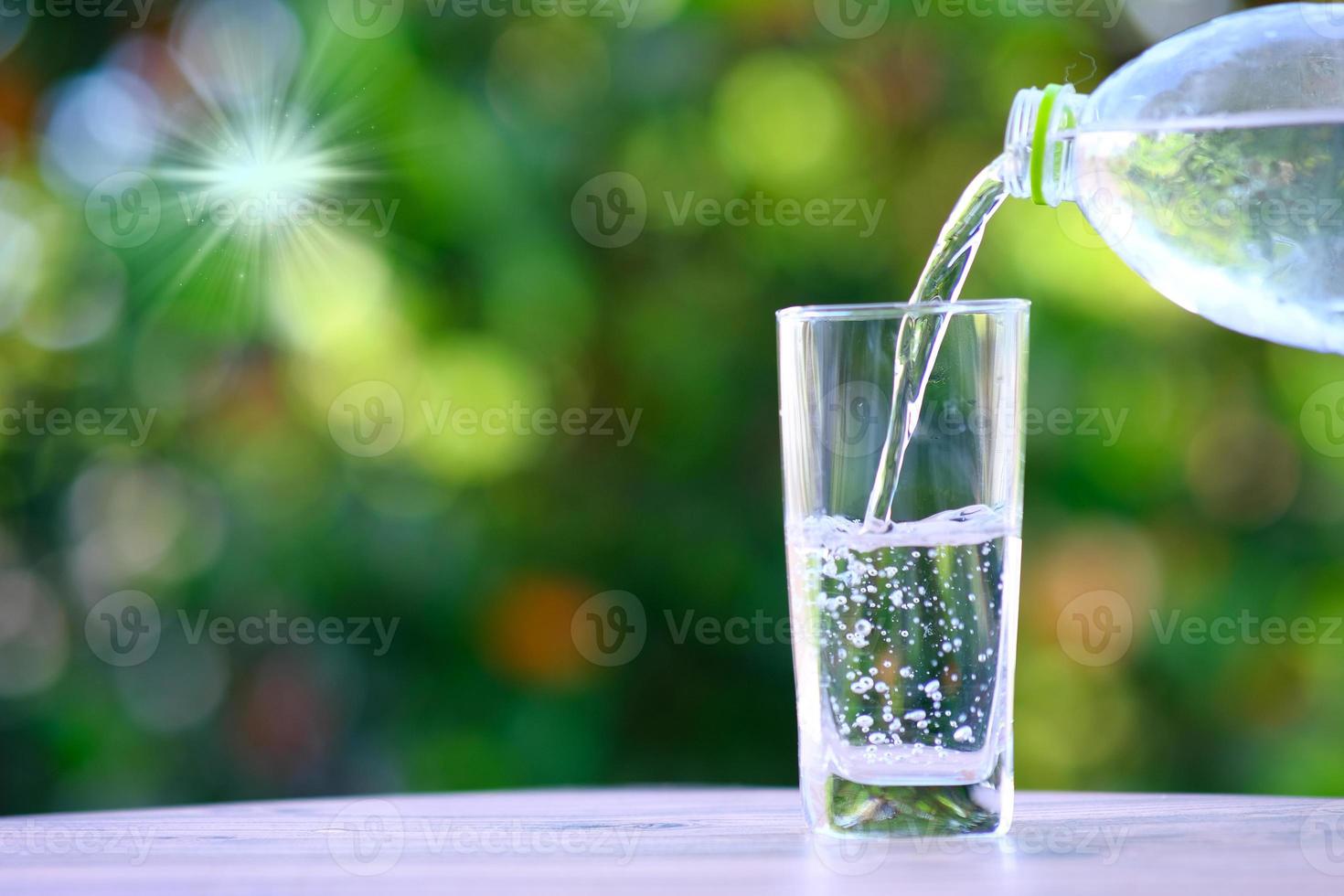 Gießen von gereinigtem frischem Trinkwasser aus der Flasche auf Holztisch und Mineralwasser-Gesundheitskonzept foto