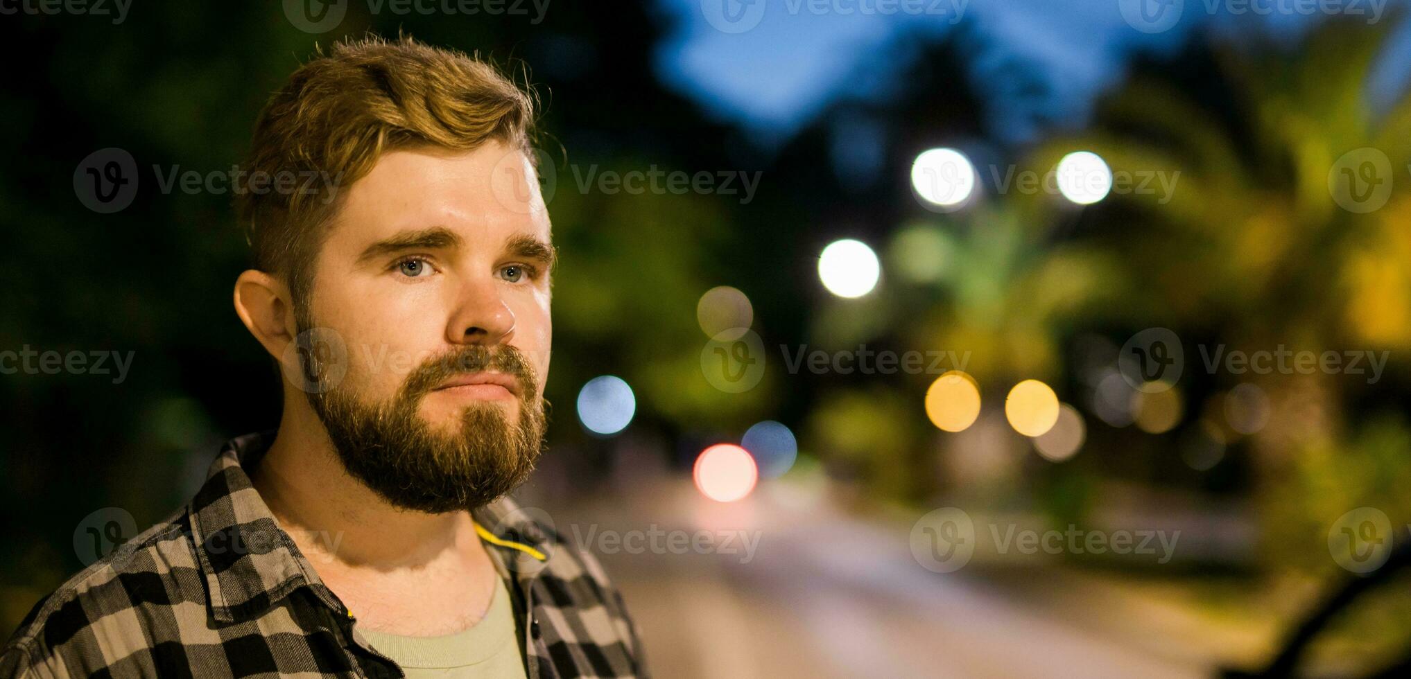 Banner Porträt von Mann Stehen im Nacht Stadt Straße mit Bokeh Straße Beleuchtung im Hintergrund. zuversichtlich einsam Kerl. Nahansicht Porträt foto