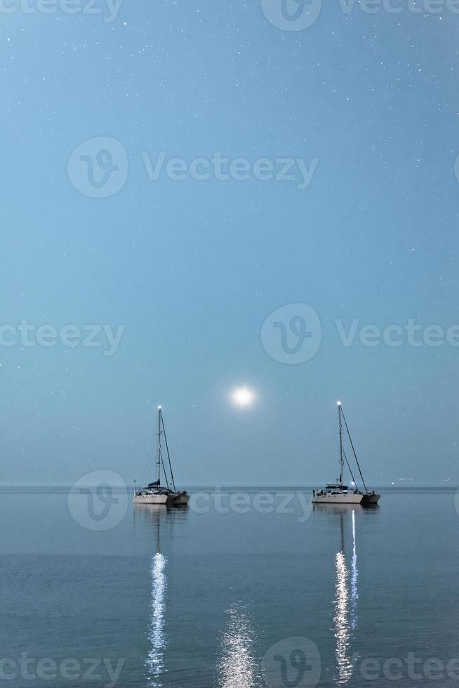 zwei Boote über dem Mondschein. zwei verankerte schiffe im offenen meer im mondschein, halbinsel kassandra, griechenland. foto