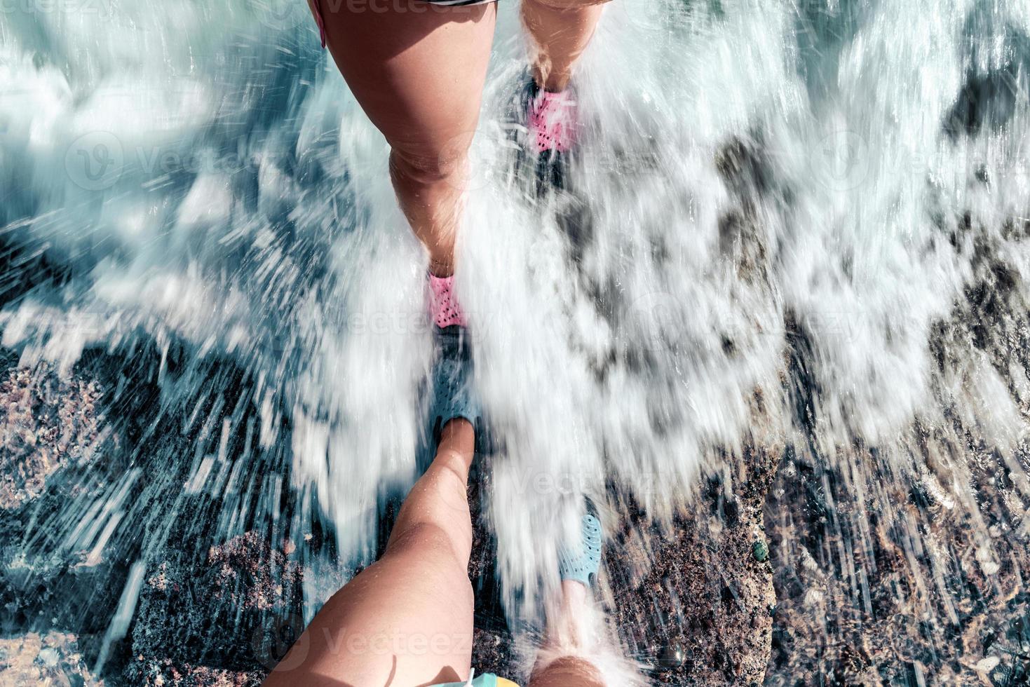 Paar steht zusammen am steinernen Ufer. Füße des Paares bedeckt von Wasserwelle am Meer. foto
