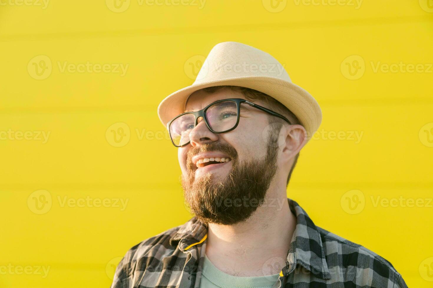 gut aussehend Kerl Tourist Lachen glücklich tragen Stroh Hut zum Reisen, Stehen gegen Gelb Mauer Hintergrund draußen foto