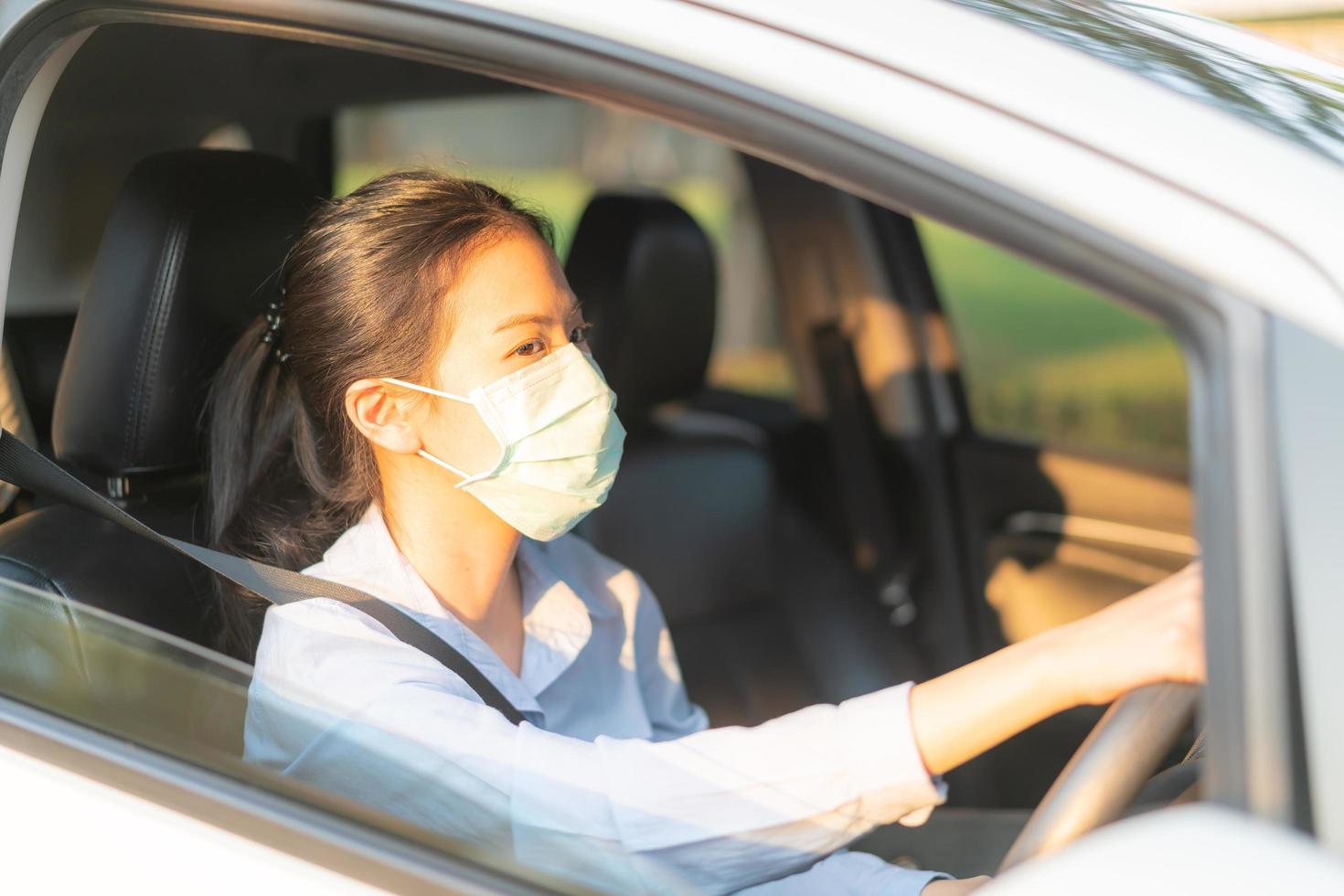 Schöne asiatische Frau, die Auto mit Gesichtsmaske fährt und nach draußen geht, bleibt gesund und schützt vor dem Coronavirus Covid-19-Virus foto