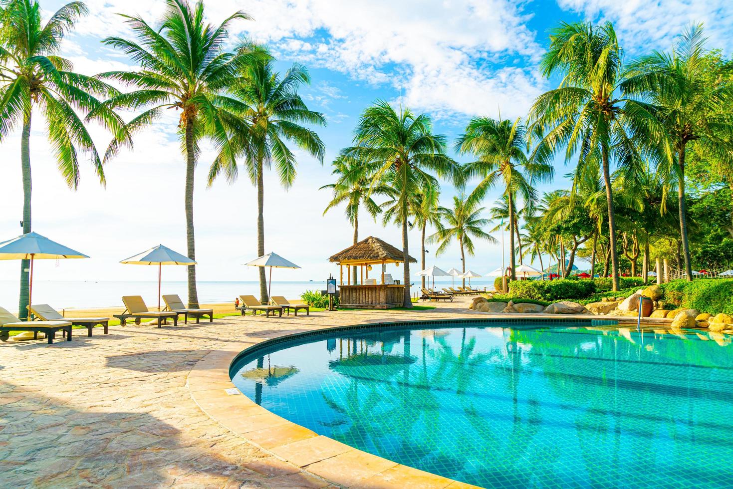 Wunderschöner Luxus-Sonnenschirm und -Stuhl um den Außenpool im Hotel und Resort mit Kokospalme am blauen Himmel foto