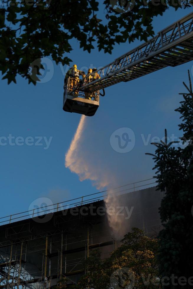 Feuerwehrleute klettern Leiter gegen Bau und Löschen eines Brandes foto