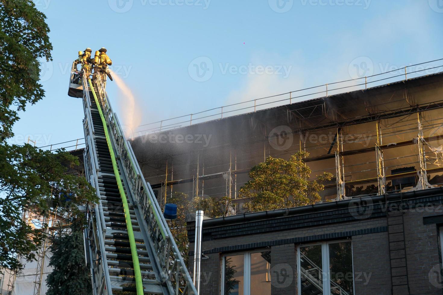 Feuerwehrleute klettern Leiter gegen Bau und Löschen eines Brandes foto