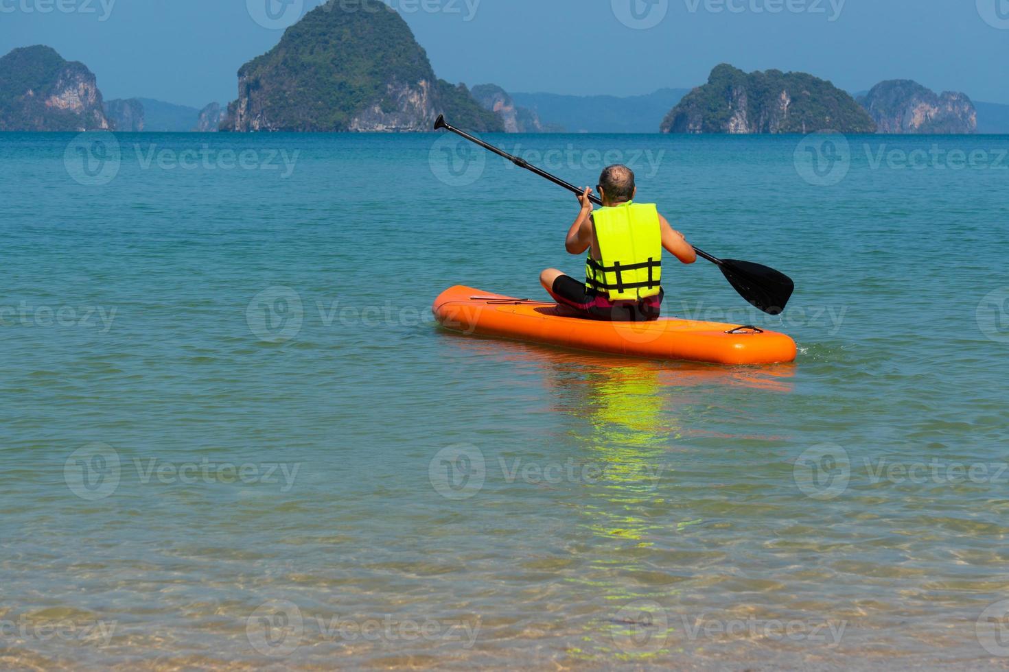 Älterer asiatischer Mann, der während der Sommerferien Paddle-Board im blauen Meer spielt foto