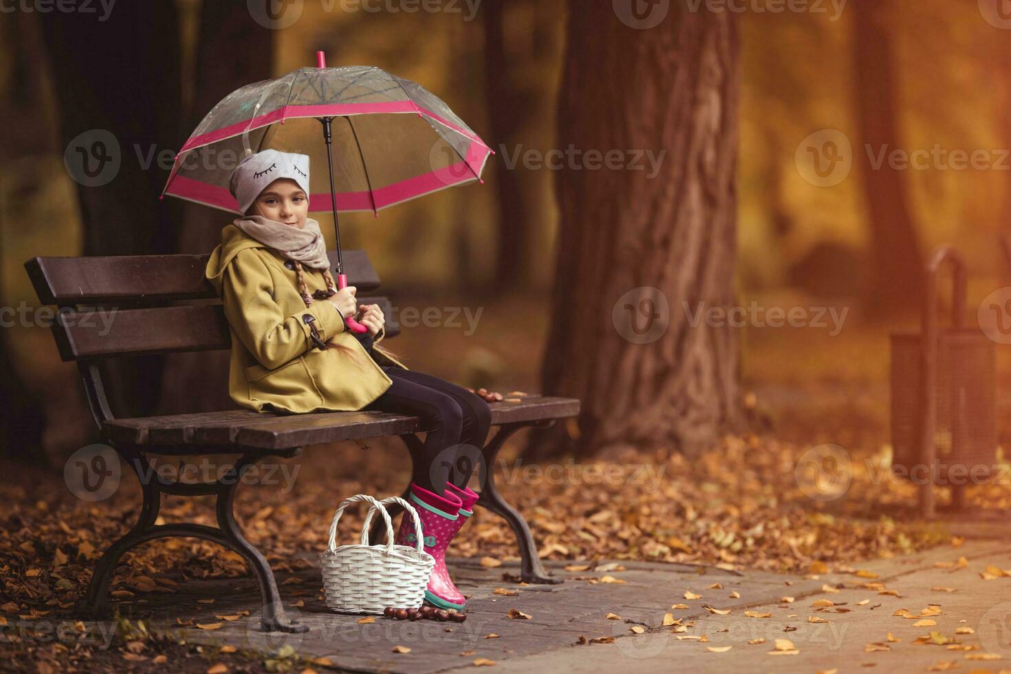 wenig Mädchen mit ein Regenschirm und ein Korb auf ein Park Bank foto