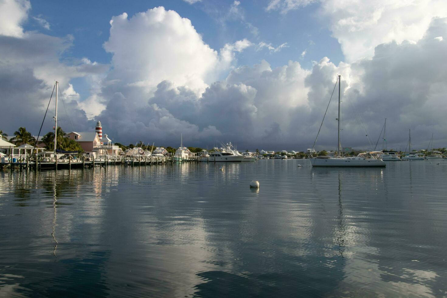 hoffen Stadt, Ellbogen Cay, Bahamas, kann 16, 2023 Boote festgemacht im das Hafen mit das Ellbogen Riff Leuchtturm im das Hintergrund während das regnerisch Jahreszeit foto