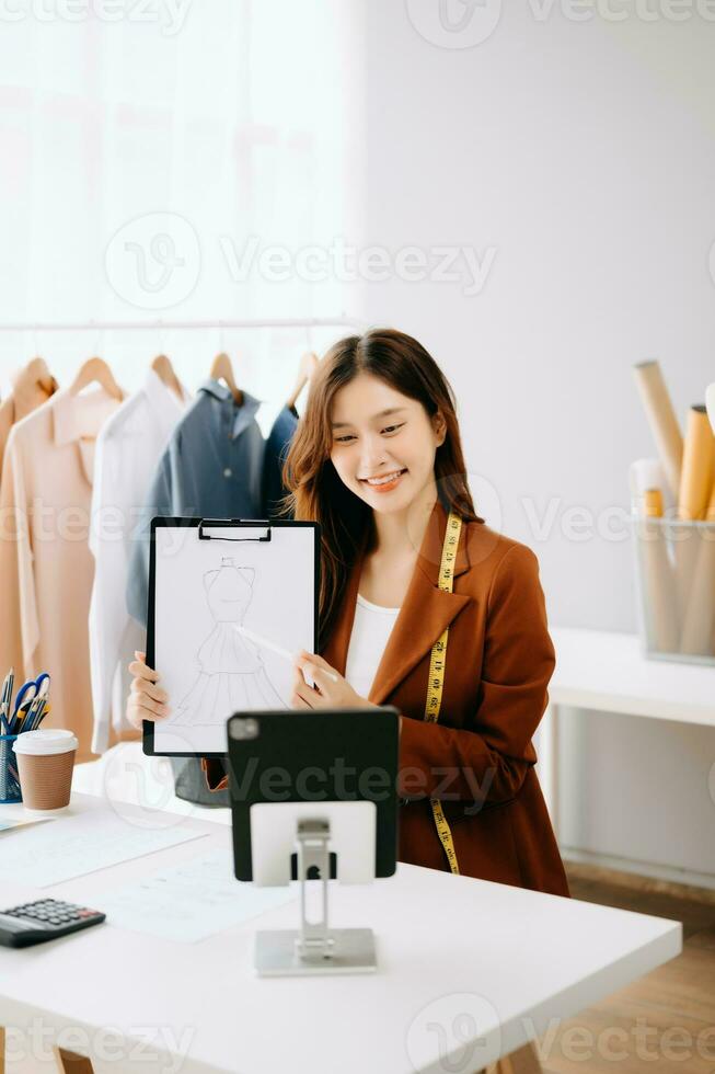 asiatisch Schneider Frau Arbeiten auf Kleider im Schneiderei Atelier. schön jung weiblich Mode Designer Lächeln und nach Erfolg im Studio foto