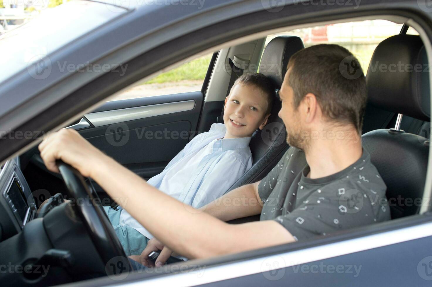 Papa sitzt mit das Kind im das Auto und hält das Lenkung Rad. Kind im das Vorderseite Sitz foto