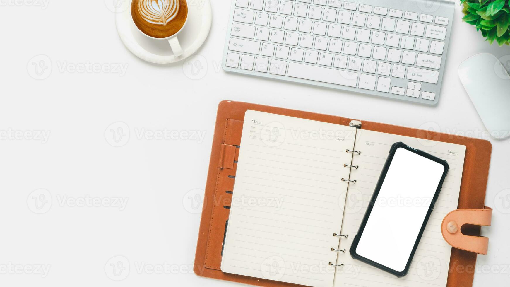 oben Sicht, Weiß Büro Schreibtisch mit Tastatur Computer, leer Bildschirm Clever Telefon, Tasse von Kaffee, Stift und Notizbuch, Kopieren Raum, spotten hoch. foto