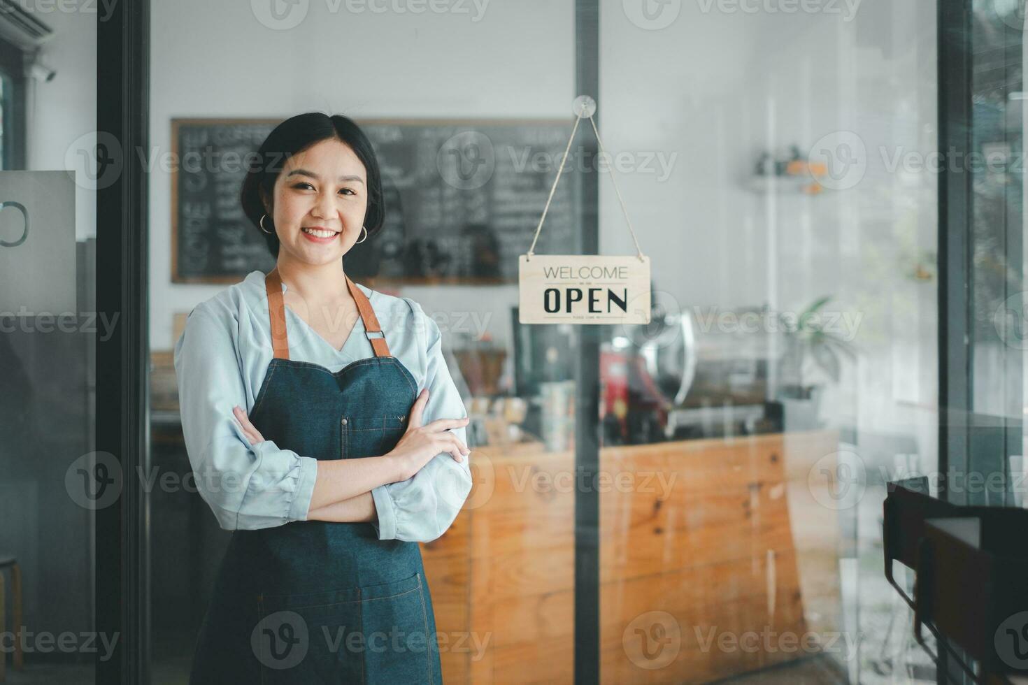 Porträt von glücklich Kellnerin Stehen beim Restaurant Eingang mit öffnen Zeichen, Porträt von jung Geschäft Frau besuchen Neu Kunden im ihr Kaffee Geschäft. foto