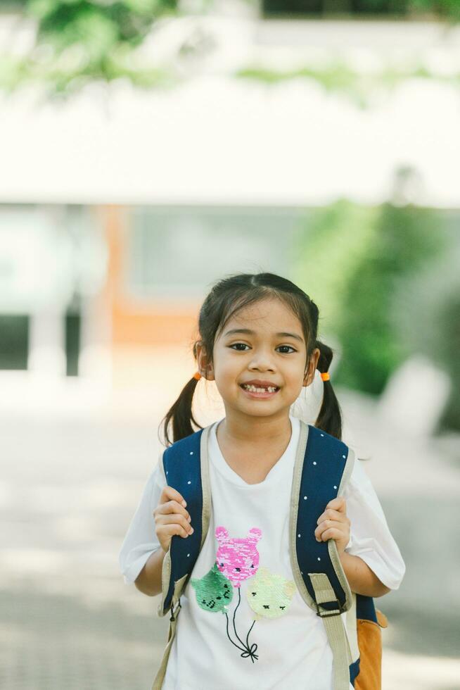 wenig asiatisch Mädchen gehen zurück zu Schule mit Rucksack und glücklich lächelnd. foto